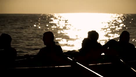 silueta del trabajo en equipo de remo y el esfuerzo que impulsa el barco en el agua al atardecer