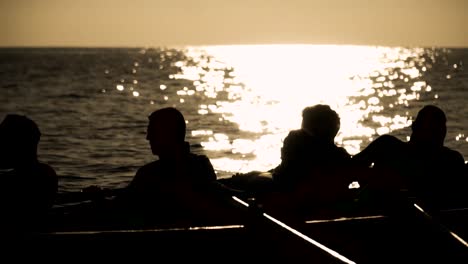 silhouette of rowing team work and effort propelling boat on water at sunset