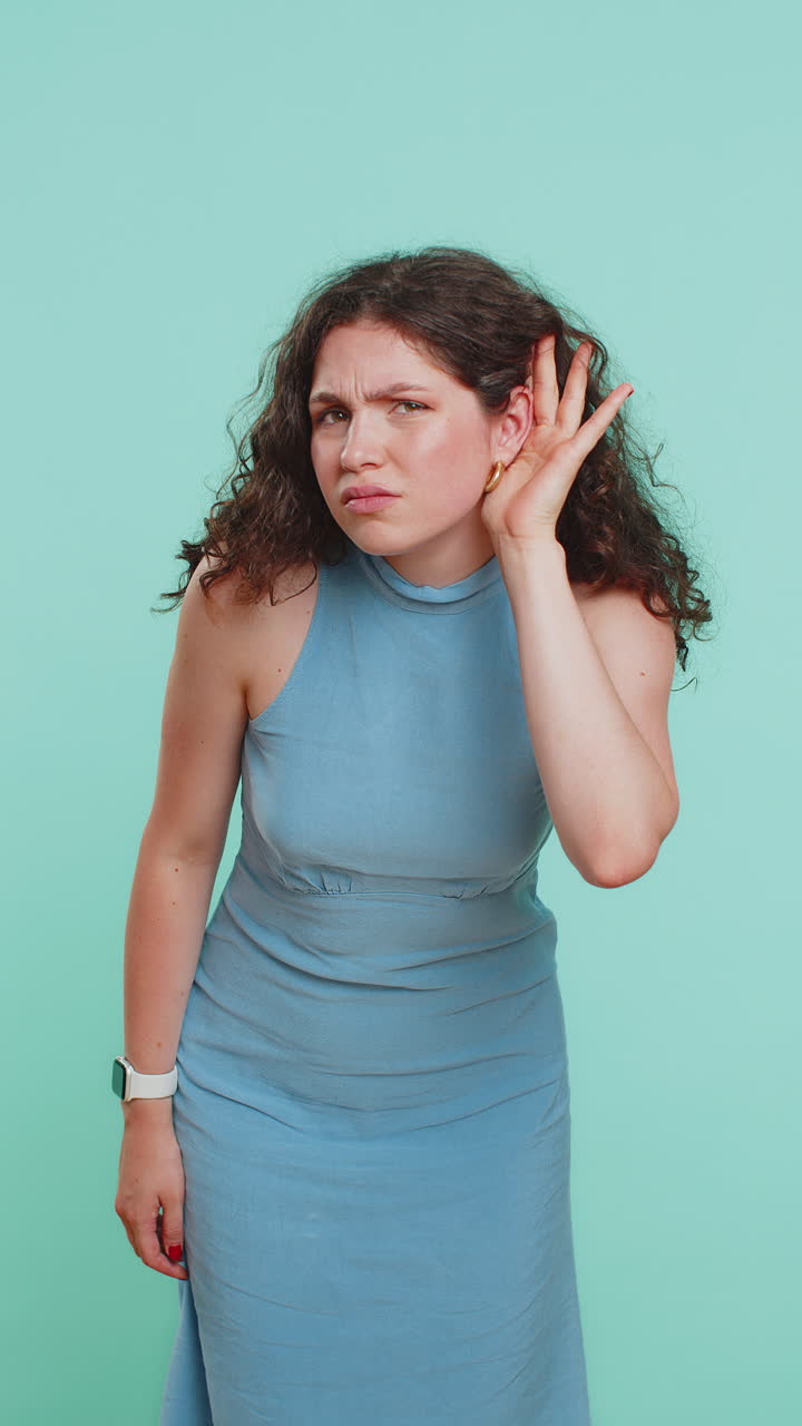 Young woman trying hear you looking confused and frowning keeping arm near ear for louder voice