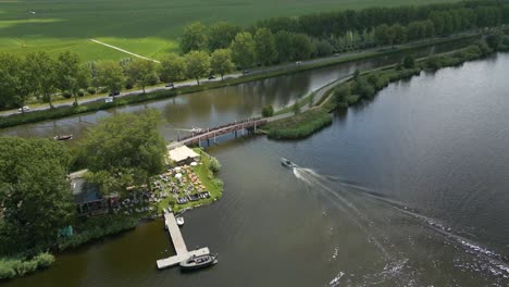 drone view of a small pier and speedboat on a lake in alphen aan den rijn, surrounded by farmland and green dikes