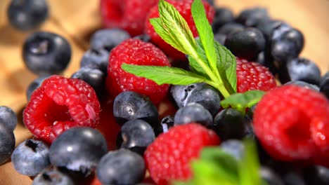 fresh raspberries and blueberries. assortment of berries and mint leaf on wooden table. 4k