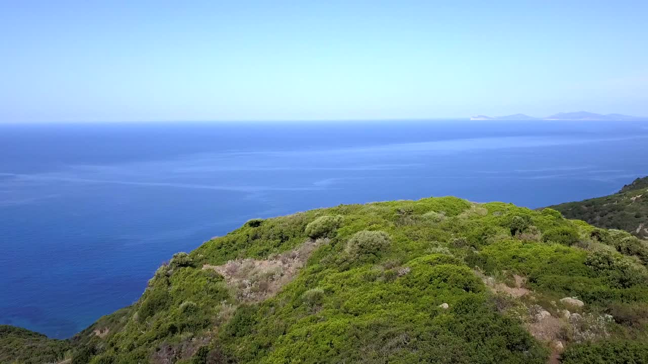 Drone Aerial shot, flying over a cliff covered in green vegetation towards a wonderful blue Mediterranean Sea along the coast of Sardinia in Italy
