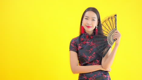 asian woman in chinese traditional costume dress holding black lace hand fan, isolated on yellow background