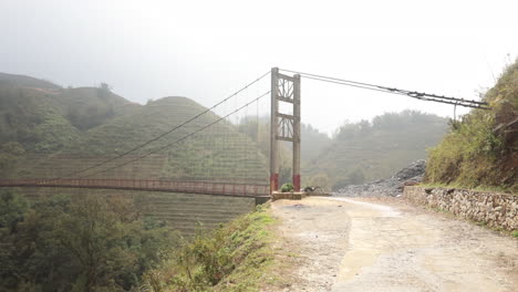 suspension bridge over misty hills in rural vietnam with a dirt road leading to it, creating a tranquil scene