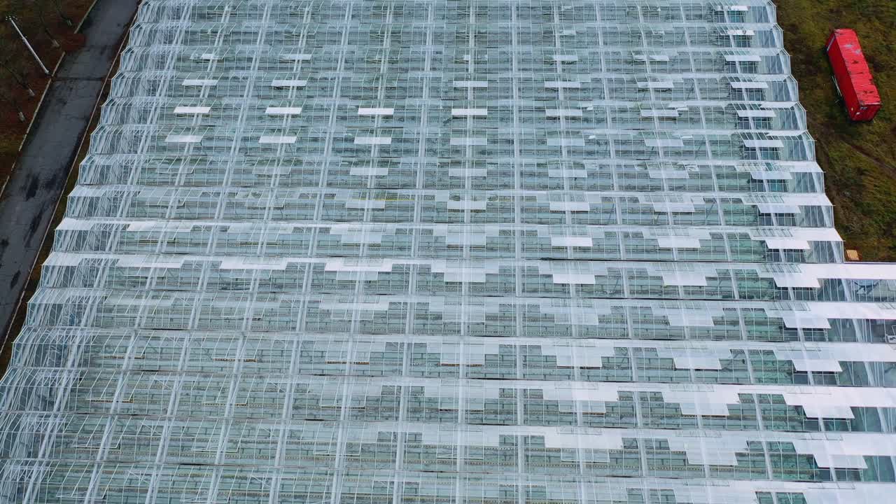 Aerial drone view of large glass windows on the roof of the greenhouse. Farming, agriculture industry. Flying over large industrial greenhouses at sunny day