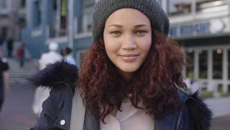 portrait of beautiful mixed race woman with frizzy hair smiling confident wearing fur coat beanie hat in busy urban background