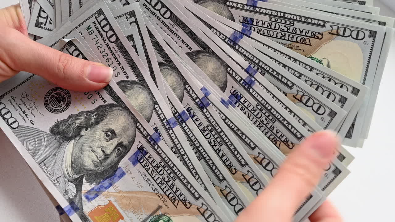 Close up of female hands holding a wide fan of one hundred dollar bills