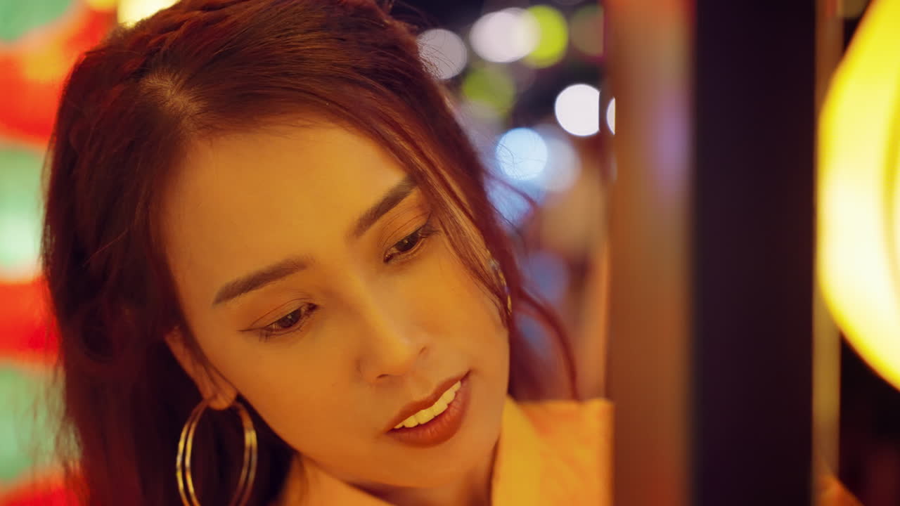 아오다이의 한 여성이 흥미로 눈을 뜨고, 베트남의 호이안에서 활기찬 불빛으로 조명됩니다.