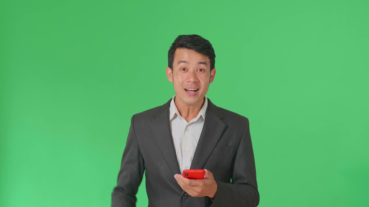 Young Asian Business Man Celebrating With Mobile Phone While Standing On Green Screen In The Studio