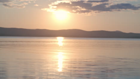 close up view of the lake and side view of a man with cap and lifejacket paddling a canoe at sunset