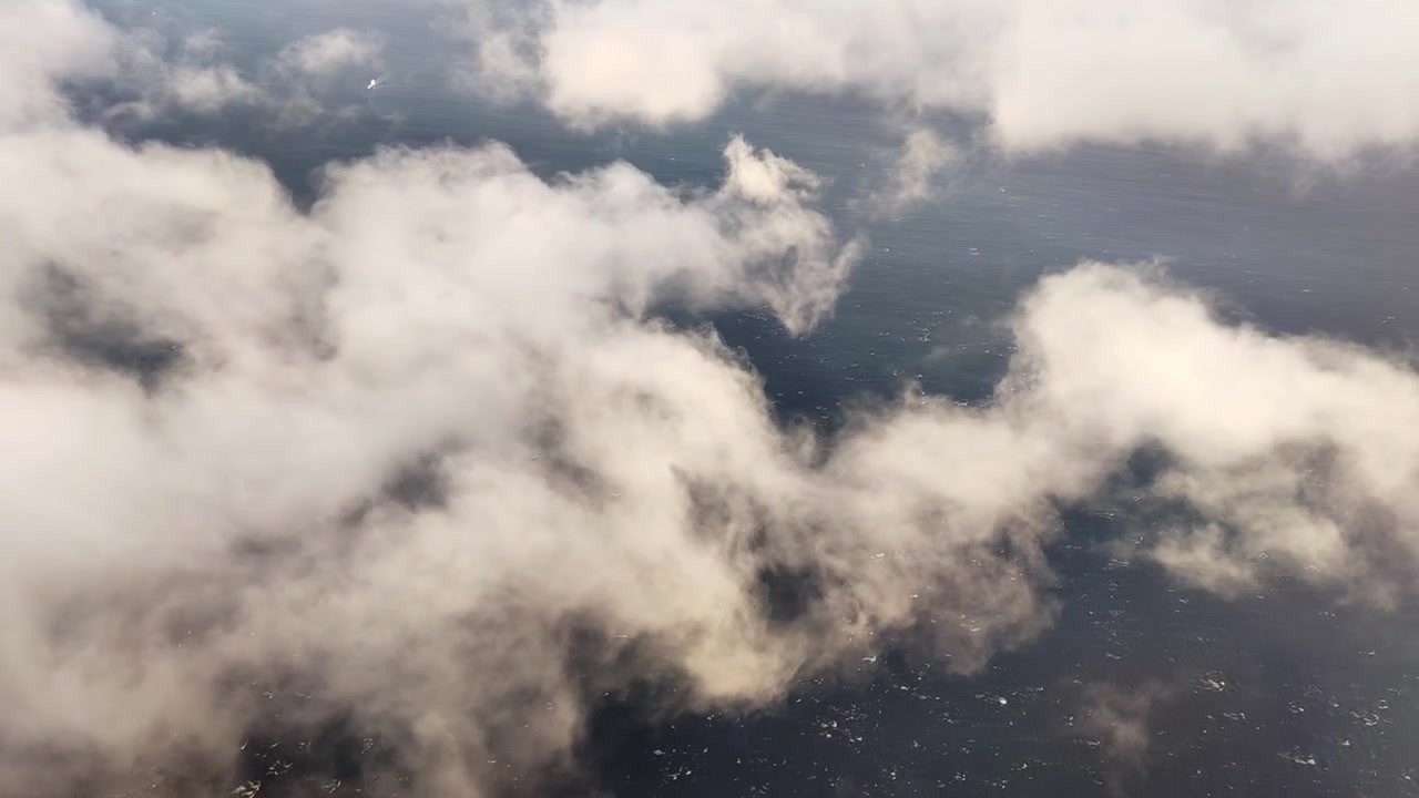 Vista dal finestrino dell'aereo su un mare ventoso con onde biancheggianti. Le nuvole passano mentre l'aereo avanza.