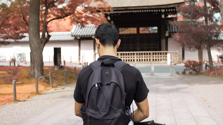 Un ragazzo che cammina attraverso le bellissime foglie autunnali arancioni verso un santuario a Kyoto, Giappone, illuminazione soffusa