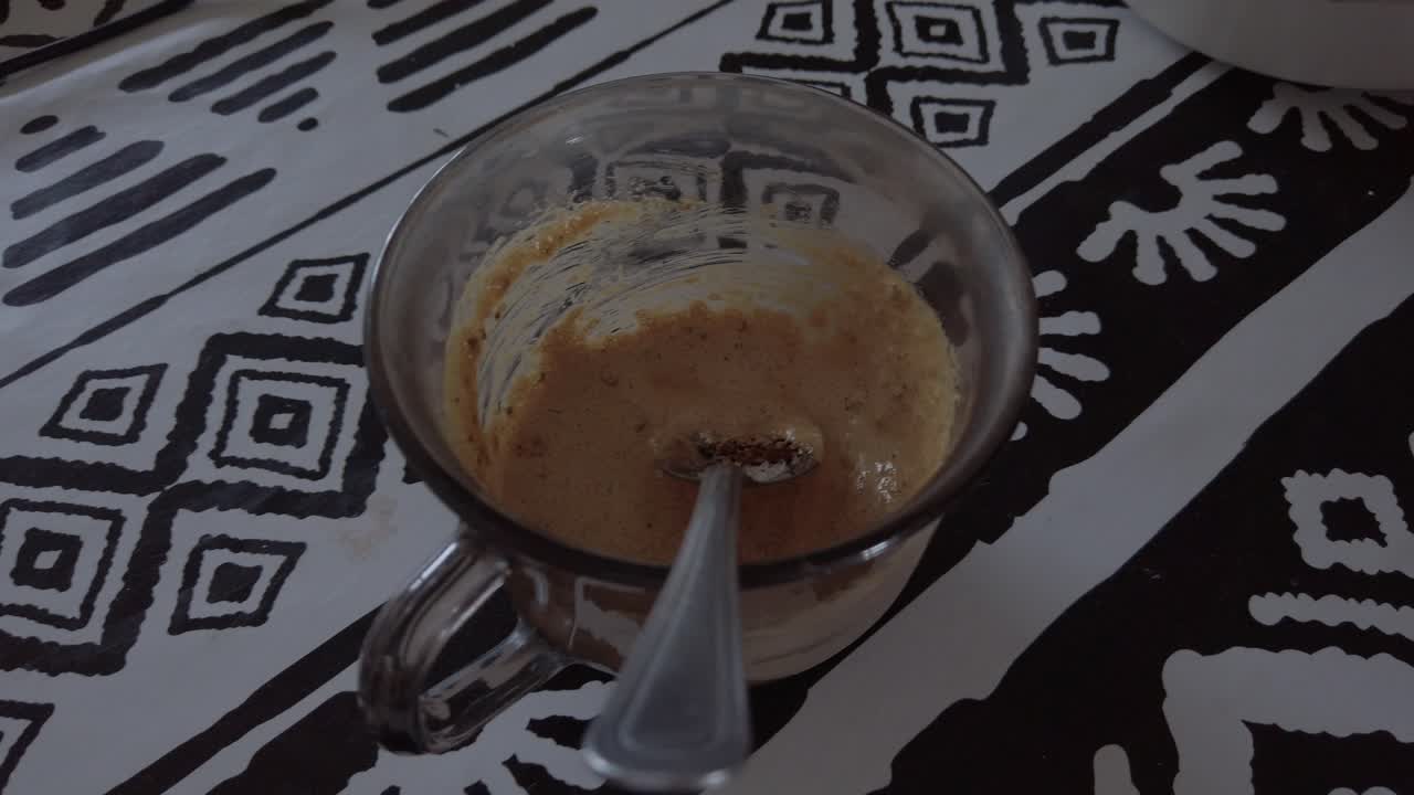 A mug of food is sitting on a table with a spoon in it