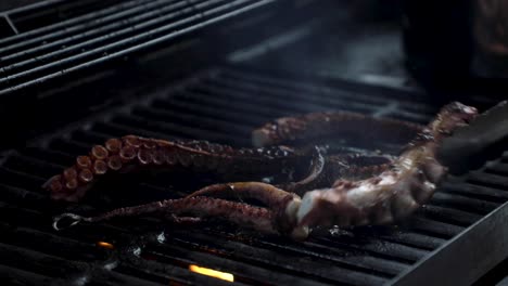 a chef pours oil over cooking octopus on an open grill, flames flare up