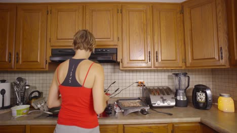 a caucasian woman places a strip of bacon onto a griddle that is filled with bacon