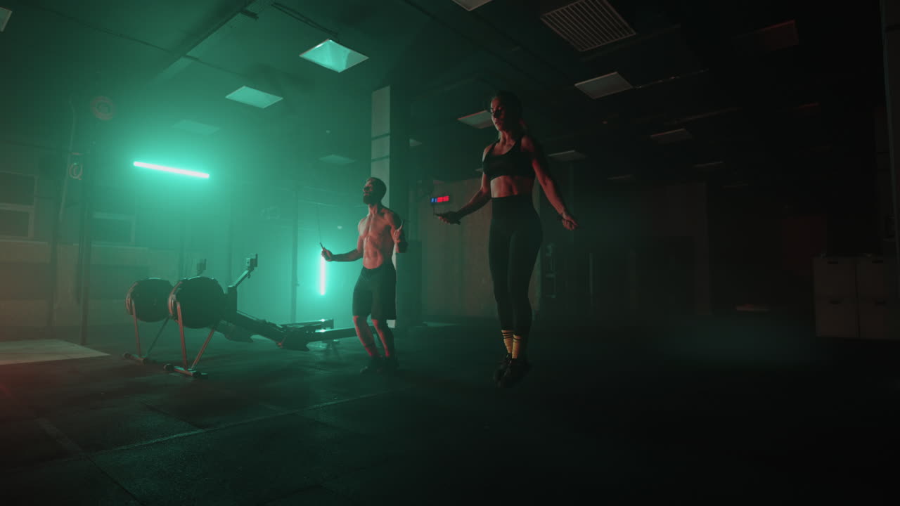 Strong man and woman jump rope together in neon light in the gym