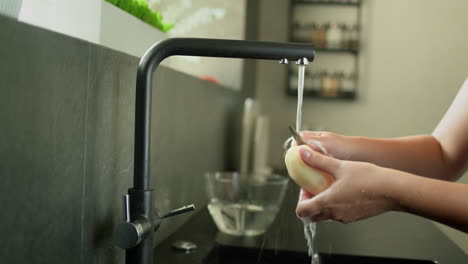 Women's-hands-under-running-water-from-a-tap-peel-potatoes