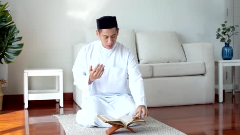 이슬람 옷을 입은 젊은 이슬람 남자가 꾸란을 읽고 기도하고 있습니다.