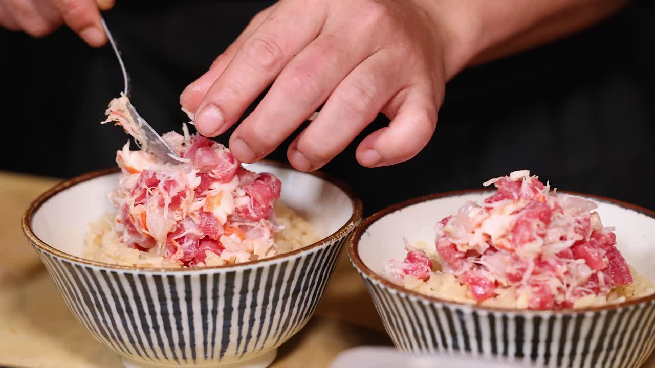 Um chef coloca cuidadosamente carne de caranguejo fresca em tigelas de arroz em um ambiente de cozinha profissional