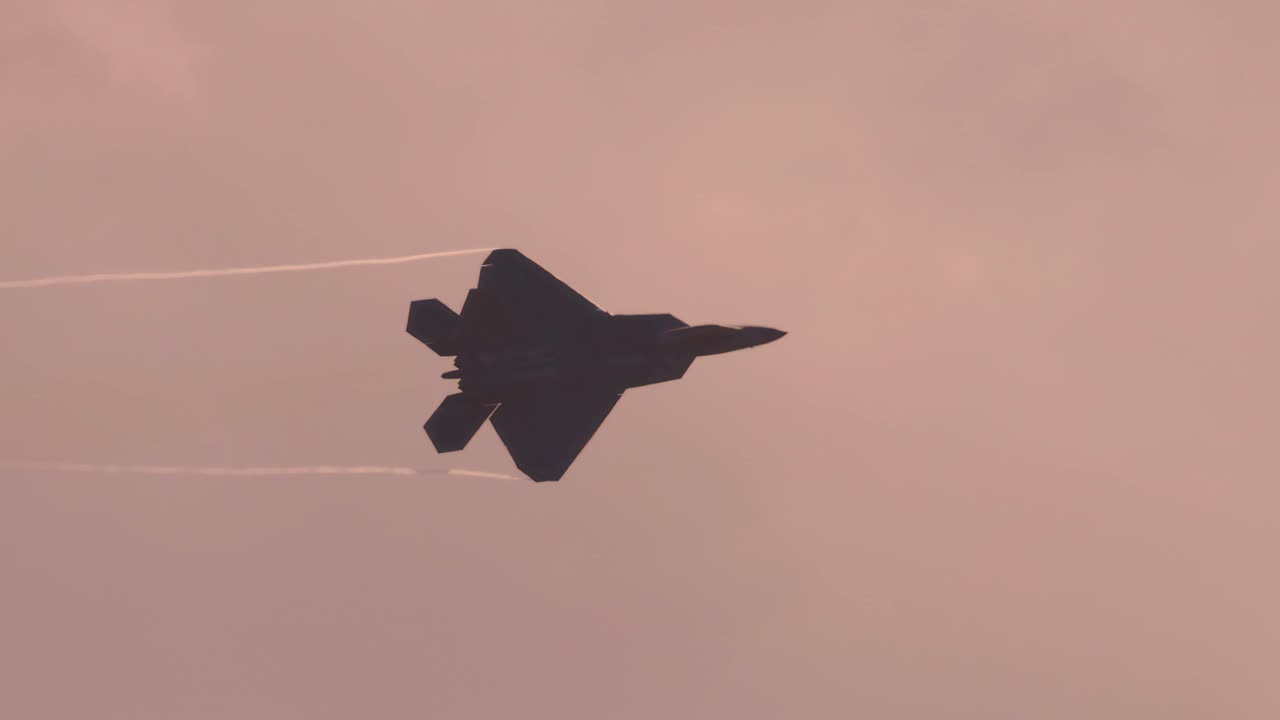 F-22 Raptor performs aerial maneuvers against a cloudy sky, showcasing speed and agility with contrails visible