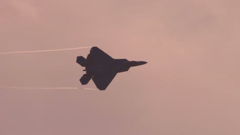 f-22 raptor performs aerial maneuvers against a cloudy sky, showcasing speed and agility with contrails visible
