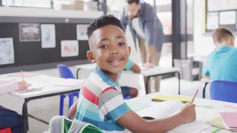 Porträt-Eines-Afroamerikanischen-Schuljungen,-Der-Im-Klassenzimmer-Lächelt-Und-Schreibt