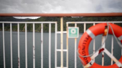 boya de vida fuera de foco en la baranda lateral de un gran barco navegando a través de exuberantes fiordos en nueva zelanda