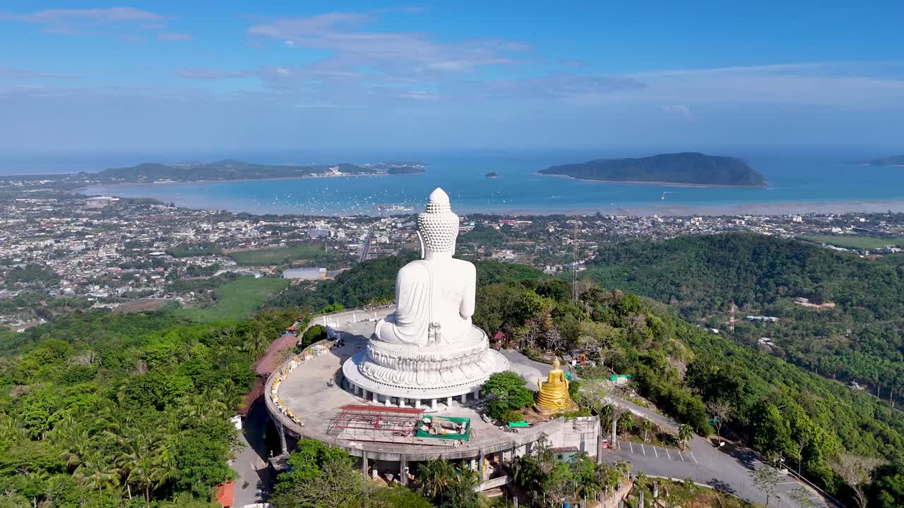 воздушные кадры, показывающие большую статую будды в пхукете, таиланд, окруженную пышной зеленью и панорамным видом на океан