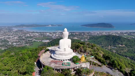 imágenes aéreas que muestran la gran estatua de buda en phuket, tailandia, rodeada de exuberante vegetación y vistas panorámicas al océano