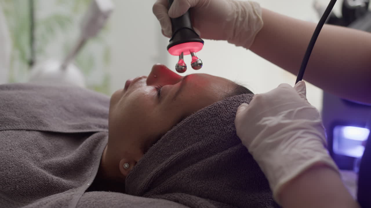 Beautician Rolling Skin Face of Client with Red Light Massage Instrument