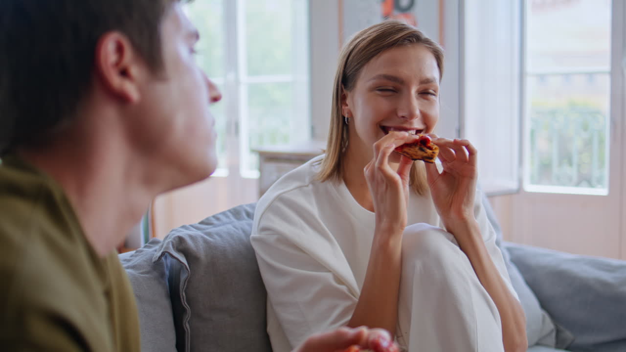 Two youngsters eating pizza watching movie in apartment closeup. Happy couple