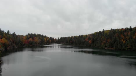 Imágenes-Aéreas-Lentas-Y-Bajas-Sobre-El-Lago-Rosa-En-Gatineau-Quebec-Con-árboles-A-Ambos-Lados-En-Hermosos-Colores-Otoñales-Y-Un-Cielo-Gris