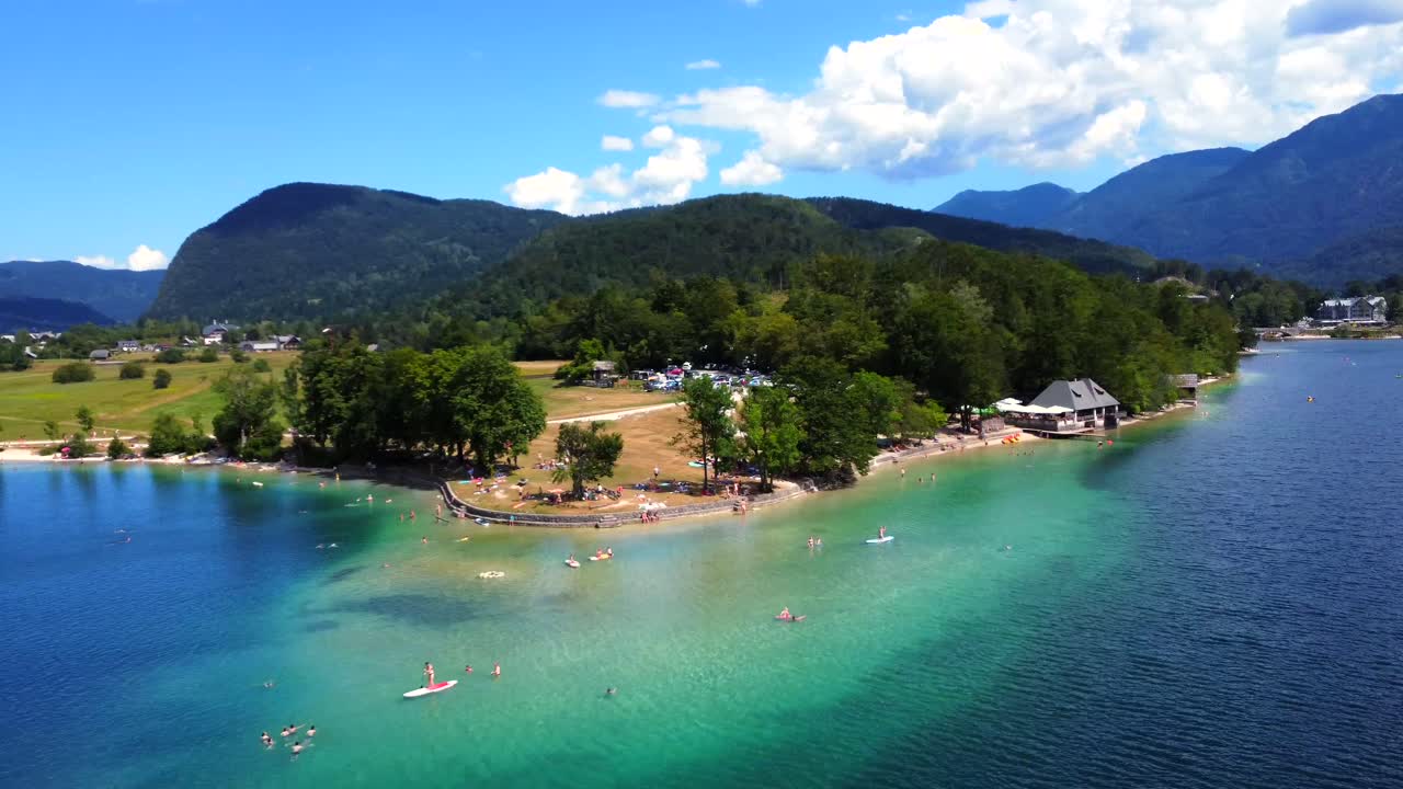 Vista aerea di un lago con montagne, alberi e persone che si godono la spiaggia