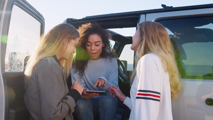 Tre ragazze in viaggio in auto che usano un tablet vicino alla loro auto.