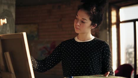 fully concentrated sophisticated female artist in her 20's is drawing picture on easel.