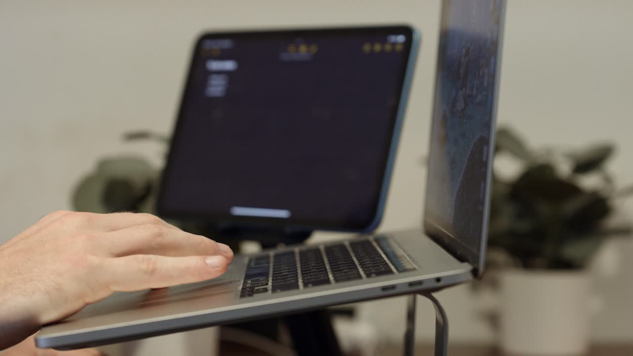Person åbner en bærbar computer på et laptopstativ. Tablet i baggrunden. Hjemmearbejde.