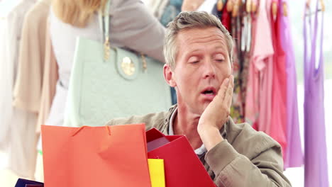 hombre aburrido con bolsas de compras sentado frente a su novia
