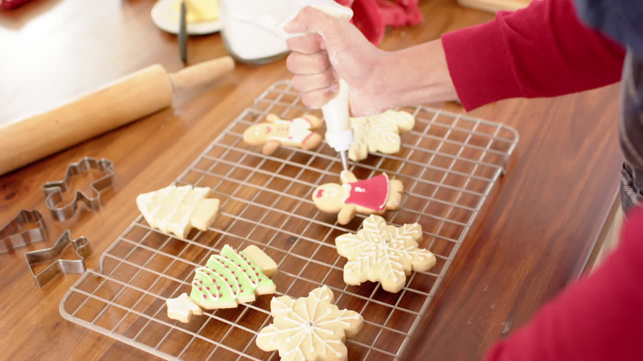 hombre biracial decorando galletas de navidad en la cocina en casa, en cámara lenta