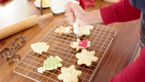 biracial man decorating christmas cookies in kitchen at home, slow motion