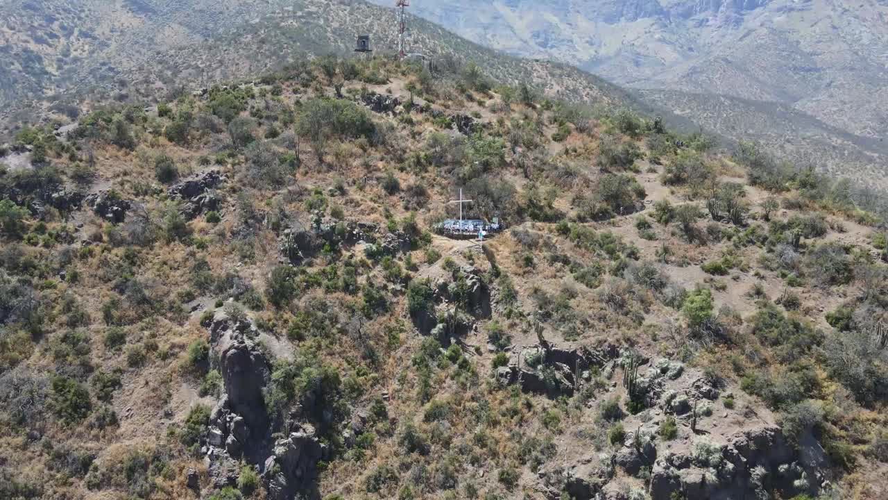 Aerial view progressively moving away from a small church on a hilltop, revealing the surrounding mountains