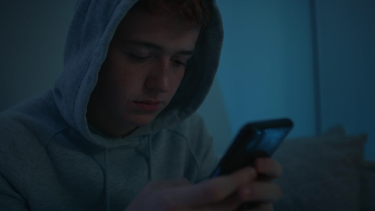 Focus caucasian teenage boy using mobile phone while sitting at night in his room