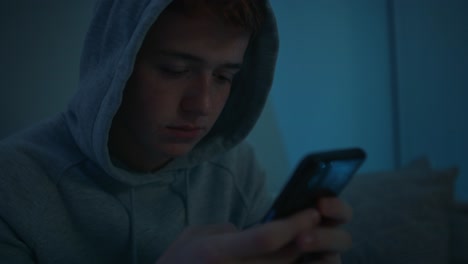 enfoque adolescente caucásico usando teléfono móvil mientras está sentado por la noche en su habitación