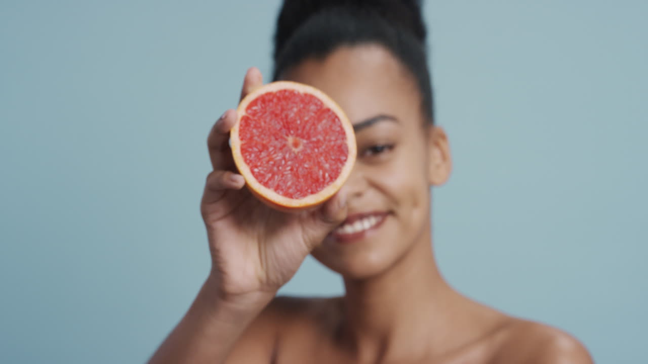 ritratto attraente giovane donna afroamericana che tiene in mano un pompelmo sorridendo godendo di un'essenza naturale di cura della pelle sana donna bella con una carnagione perfetta sullo sfondo blu