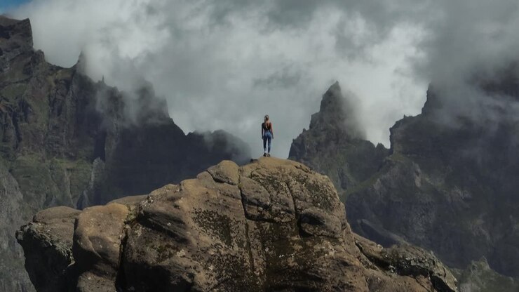 Donna in forma sta in piedi con sicurezza su una piccola cima di montagna che si affaccia su maestose scogliere