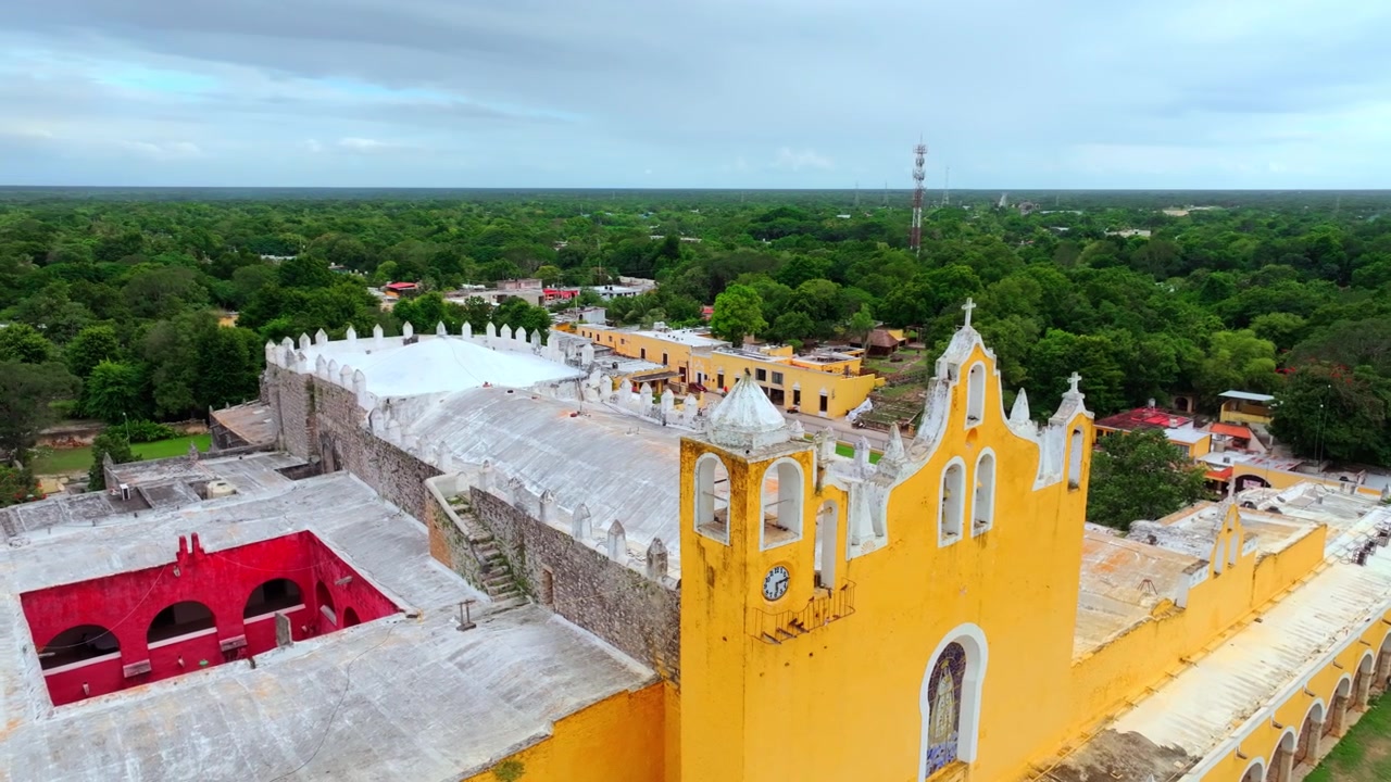 Vista aérea de la fachada amarilla de la iglesia del convento de San Antonio en Izamal, Yucatán, México, paredes ocres decoradas con estandartes rojos de festival