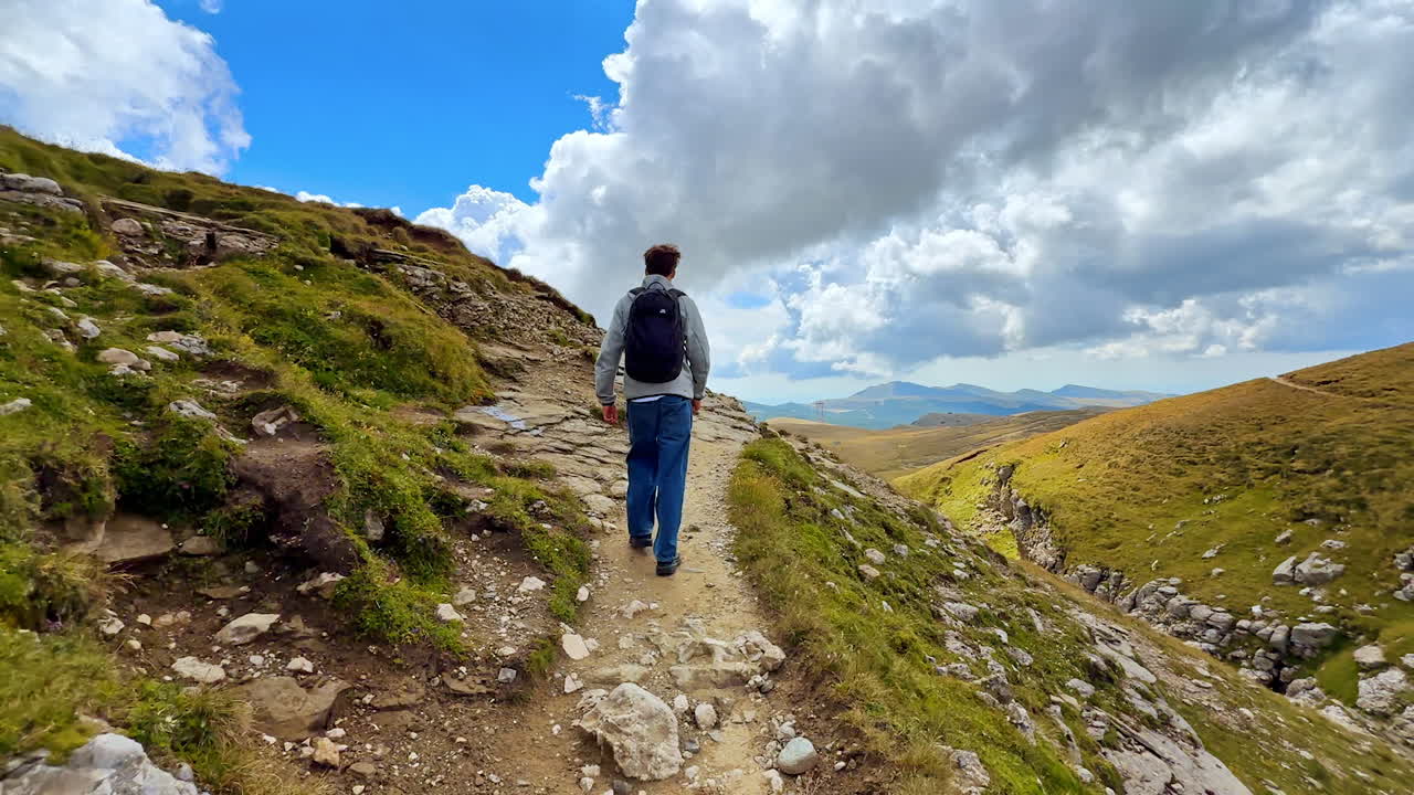 Hiker on mountain trail in Bucegi range. Person hiking along mountain trail in Bucegi Mountains with cloudy sky