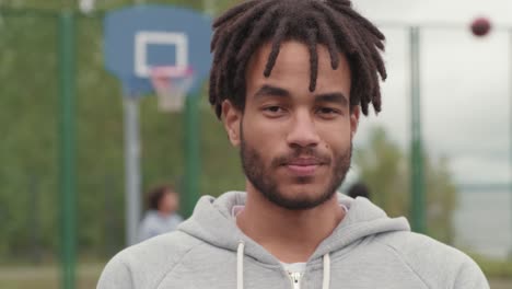 joven atleta afroamericano sonriente con rastas sosteniendo la pelota para jugar baloncesto en la cancha de baloncesto