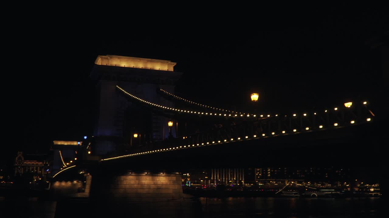 People Walking At The Szechenyi Chain Bridge Over Danube River In Budapest Hungary At Night - Panoramic Shot