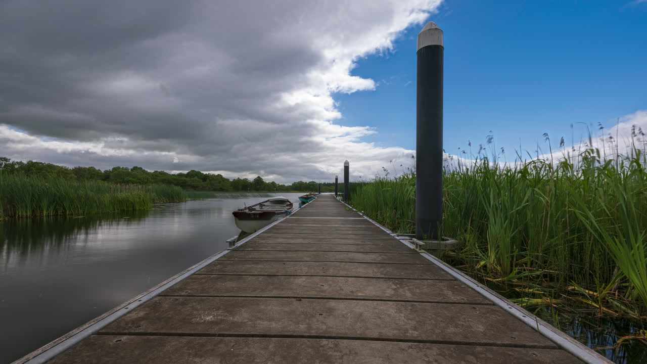 lapso de tiempo del embarcadero de madera local con barcos estacionados rodeados de juncos en lough key en el condado de roscommon en irlanda en un día soleado con nubes que pasan en el cielo durante la primavera
