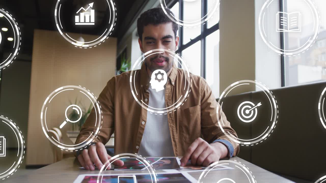 Man spreading prints in cafe booth, causing animated icons orbiting while reviewing design work